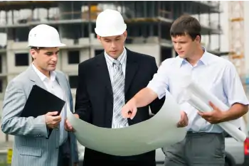 Three businessmen standing in a warehouse looking at a sheet of plans
