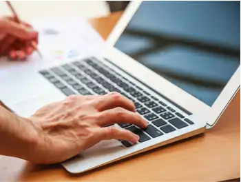 Hands working on a laptop and writing on a paper
