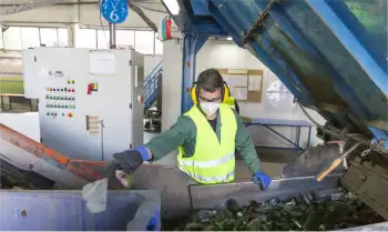 Worker wearing safety gear sorting recycling in a warehouse at a machine