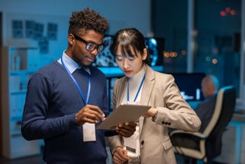 Two young interracial colleagues preparing presentation while scrolling through online information in tablet