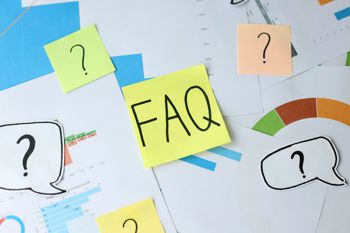 A sticky note with FAQ on it stuck on a paper with charts and question marks